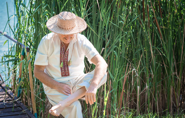 Ευτυχισμένος ηλικιωμένος άνδρας με κεντημένη φούστα και ψάθινο καπέλο στη φύση ξεκούραση, τρόπος ζωής των συνταξιούχων - Φωτογραφία, εικόνα