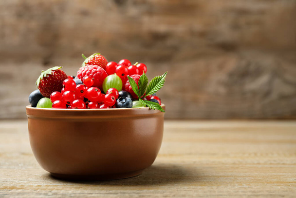 Mix of different fresh berries in bowl on wooden table. Space for text - Foto, Bild