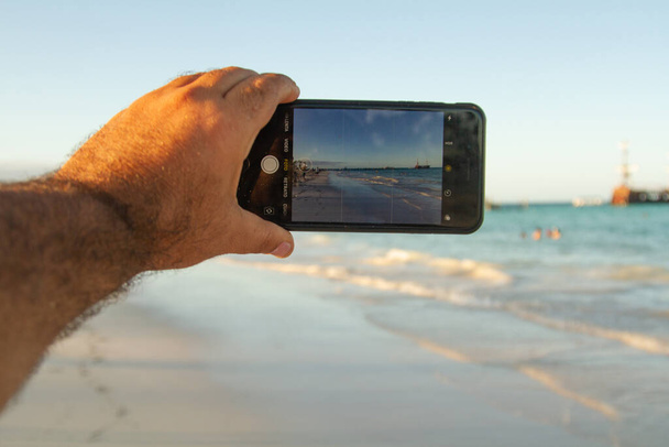Persoon die een foto neemt met een mobiele telefoon van een brug op een zonnige dag terwijl hij de parameters op het frame van de camera op het scherm bekijkt - Foto, afbeelding