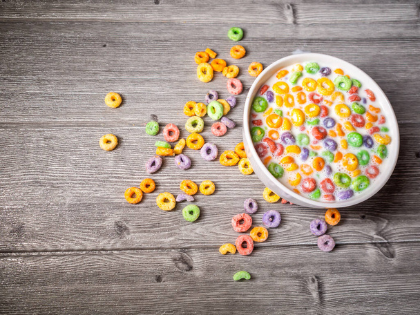 beaucoup de céréales rondes colorées avec du lait dans un bol blanc sur une vue de dessus de table grise - Photo, image
