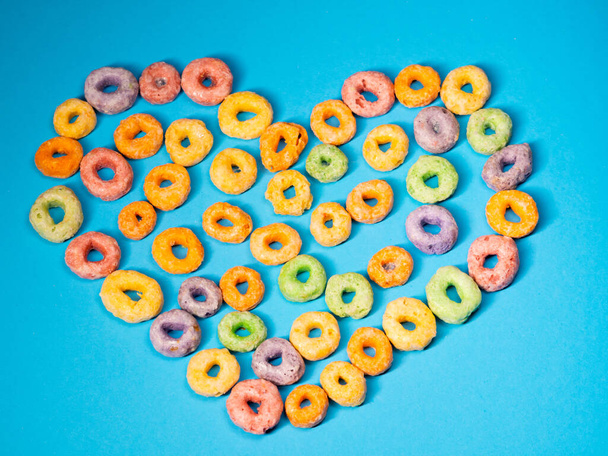 many colorful round heart shaped sugary cereal grains on a blue colored background - Photo, Image