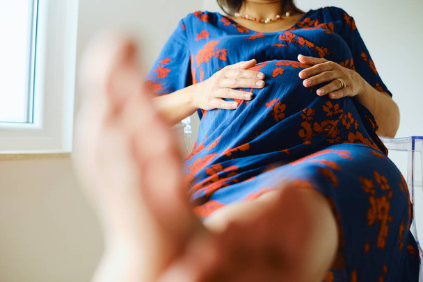 Raskaana oleva nainen istuu jalat ylös ja koskettaa vatsa - Valokuva, kuva