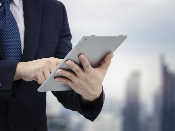 Νεαρός Ασιάτης επιχειρηματίας με στολή που χρησιμοποιεί ψηφιακό tablet στην ταράτσα με θέα στον ουρανοξύστη - Φωτογραφία, εικόνα