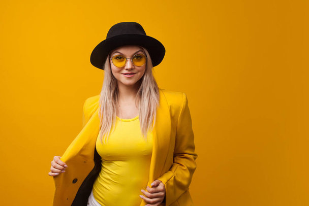 Stylish trending young woman in bright clothes on yellow background, copy space. Cool blonde - 写真・画像