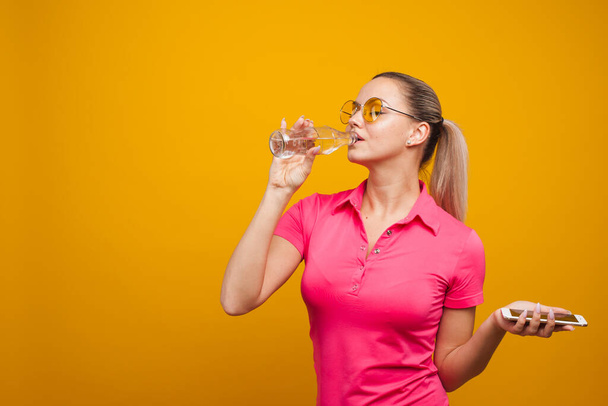 Healthy habits, an app to track the amount of water you drink. Young woman with a bottle of water and a smartphone - Фото, изображение