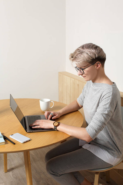 Young focused hipster millennial female with short blonde haircut working with laptop in cafe interior, close-up side view, looking at screen and typing - Foto, imagen