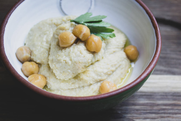 Hummus decorated with parsley and chickpea peas in a ceramic bowl on a wooden background  - Photo, Image