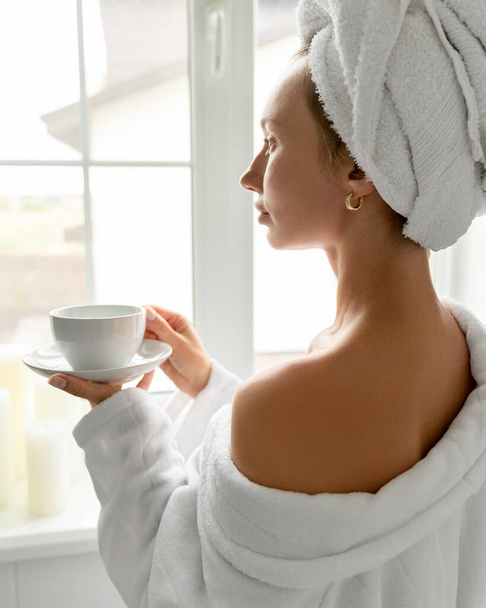 Genç kadın banyoda kahve içiyor. Cilt bakımı rutini. Yavaş yaşam, hayatın tadını çıkarmayı bırak. - Fotoğraf, Görsel