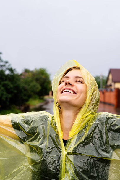 Χαρούμενη λευκή γυναίκα με κίτρινο αδιάβροχο που απολαμβάνει τη βροχή. - Φωτογραφία, εικόνα