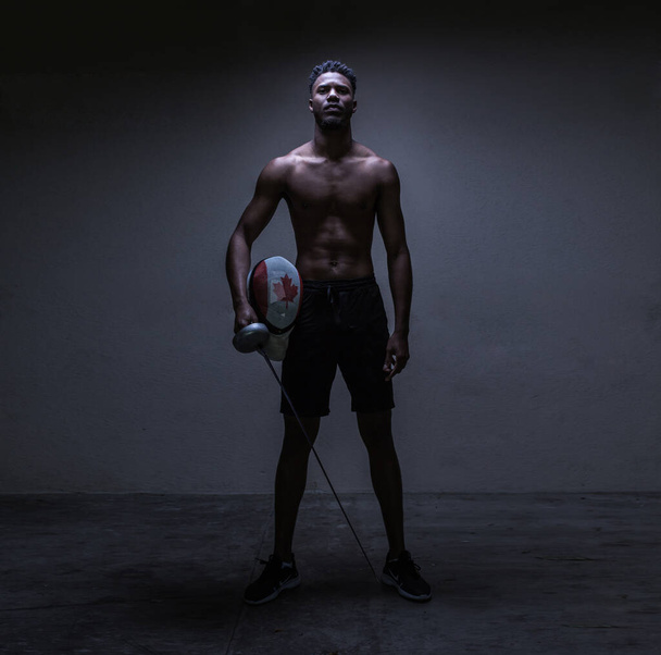 Ένα χαμηλό βασικό πλήρες πλαίσιο πορτρέτο του Καναδού αθλητή, κρατώντας τον εξοπλισμό του, ταιριάζει μαύρο άνδρα - Φωτογραφία, εικόνα