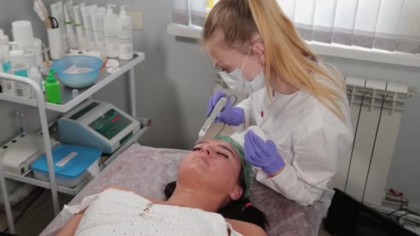 Profesyonel kozmetik uzmanı kadın hastaya ultrasonik yüz temizliği yapıyor.. - Video, Çekim