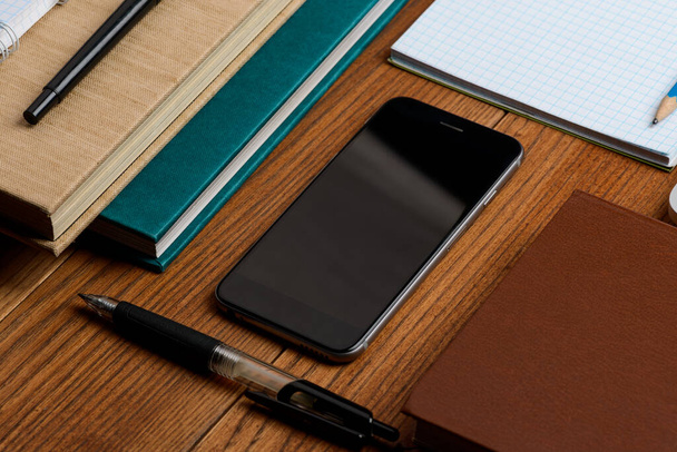 Smart phone on wooden desktop among books and stationery - Foto, Imagem
