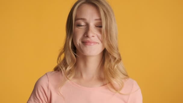 Hezké usmívající se blond dívka půvabně dívá do kamery přes barevné pozadí - Záběry, video