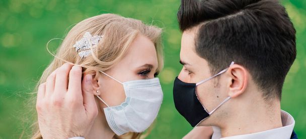 Jonge liefdevolle paren lopen in medische maskers in het park tijdens quarantaine op hun trouwdag. Coronavirus, ziekte, bescherming, ziek. Europese viering geannuleerd. - Foto, afbeelding