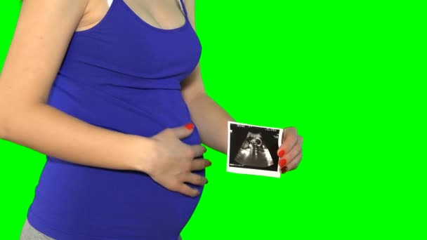 妊娠中の女性の腹と手は小さな妊娠写真を保持します。クロマキー画面。4K - 映像、動画