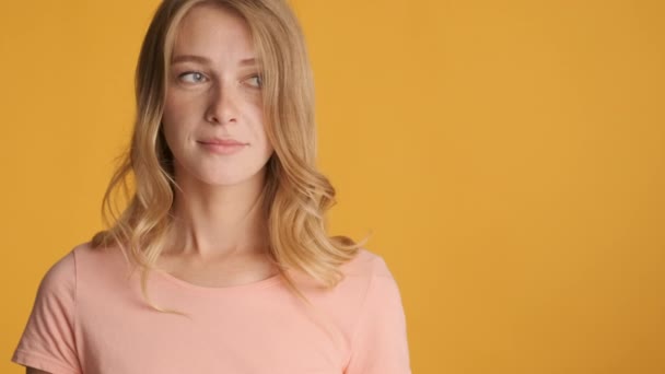 Hübsches fröhliches blondes Mädchen schaut erstaunt in die Kamera und zeigt mit dem Finger auf Kopierraum neben buntem Hintergrund - Filmmaterial, Video