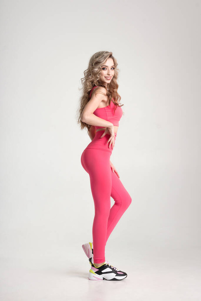 Full length portrait of attractive female in sporty shape wearing pink sportswear isolated on white background in studio. Concept of fitness coach or trainer - Zdjęcie, obraz