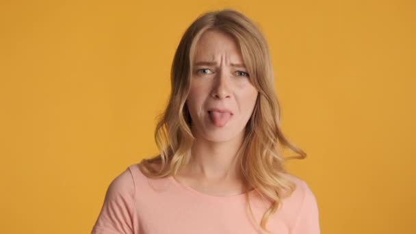 Joven atractiva mujer rubia ofendidamente mostrando la lengua en la cámara sobre el fondo colorido
 - Metraje, vídeo