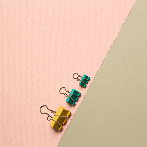 Sárga és zöld fém kötőkapcsok rózsaszín és bézs háttérrel. felülnézet - Fotó, kép