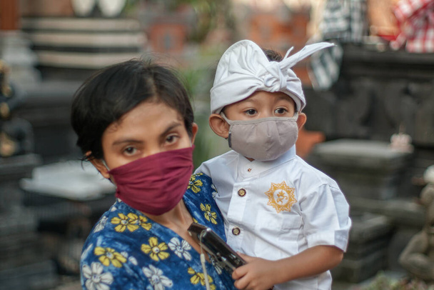 A balinéz anya és gyermek hagyományos ruhát visel a koronajárvány vagy a kovid-19 idején. Mindketten maszkot használnak, hogy megvédjék magukat a vírustámadásoktól. A templomban készülnek imádkozni. - Fotó, kép