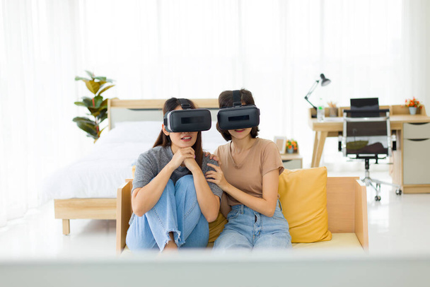 Teini-ikäiset tytöt, jotka ovat intiimejä ystäviä, joilla on VR-lasit istuessaan sohvalla, kaksi nuorta aasialaista tyttöä ovat yllättyneitä ja innoissaan virtuaalitodellisuudesta, jonka hän näki.. - Valokuva, kuva
