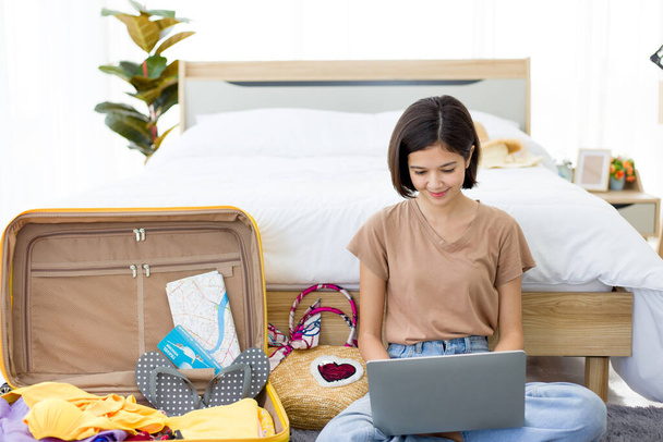 Jonge Aziatische vrouw is het boeken van kamers online op de laptop, terwijl zitten aan het einde van bed. Mooie meisjes plannen een vakantie reis in de zomer thuis. - Foto, afbeelding