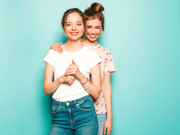 Two young beautiful blond smiling hipster girls in trendy summer hipster jeans clothes. Sexy carefree women posing near blue wall. Trendy and positive models having fun - Zdjęcie, obraz