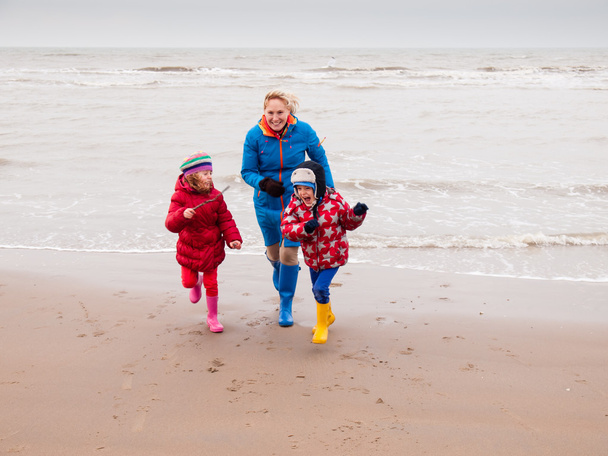 Mujer y dos niños pequeños jugando en la playa de invierno
 - Foto, imagen