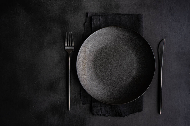 Table setting with plate, napkin and cutlery in black with copy space - Photo, Image