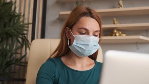 Coronavirus quarantine. Woman at the office with mask for corona virus. Business women wear masks to protect and take care of their health. Home working with computer. Working from home - Materiaali, video