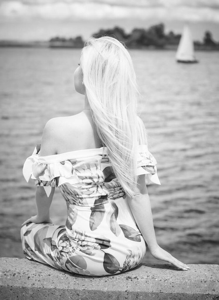Piękne blond włosy kobieta w romantycznych kwiatów sukienka w pobliżu niebieskiej wody i piasku. Cute happy girl zabawy na łonie natury w wakacje - Zdjęcie, obraz