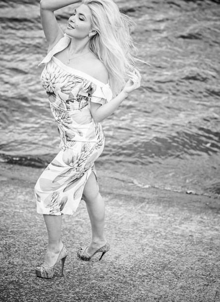 Όμορφη ξανθιά γυναίκα μαλλιά σε ρομαντικά λουλούδια φόρεμα κοντά σε μπλε νερά και άμμο. Χαριτωμένο χαρούμενο κορίτσι διασκεδάστε σε μια φύση στις διακοπές - Φωτογραφία, εικόνα