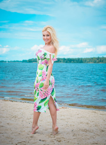 Mooie blonde haarvrouw in romantische bloemen kleden zich in de buurt van blauw water en zand. Schattig gelukkig meisje veel plezier op een natuur in vakantie - Foto, afbeelding