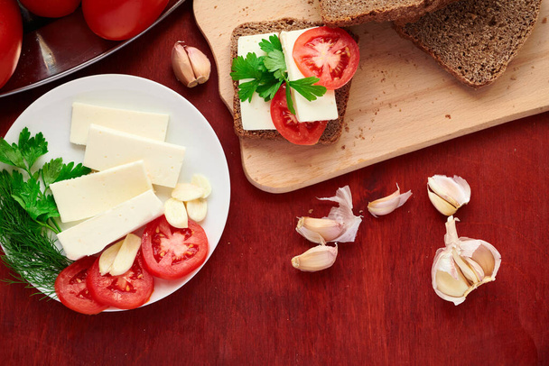здорова їжа - свіжий хліб і сир фета на дерев'яному фоні, помідори, зелень та овочі
 - Фото, зображення