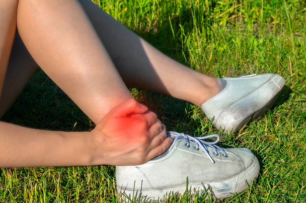 Young woman touching painful twisted ankle, woman sport running ankle sprain,legs have problem,accident, hand massaging her leg pain after exercise in outdoor park. - Photo, Image