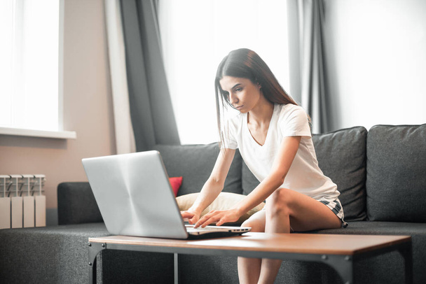 Jonge vrouw met moderne laptop zittend op de bank thuis. Gelukkig meisje surfen via het internet tijdens vrije tijd..  - Foto, afbeelding