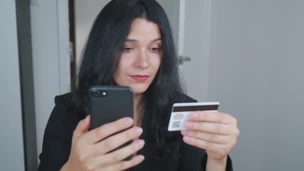 Genç bir kadın kredi kartıyla cep telefonundan alışveriş yapıyor. Gülümseyen genç bayan müşteri elinde kredi kartı ve akıllı telefon ile online mağazadan alışveriş yapıyor. E-bankacılık uygulama servisi. Sabit çekim. - Video, Çekim