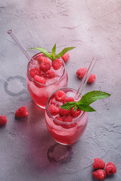 Fresh ice cold berry juice drink with mint, summer raspberry lemonade in two glass with straws on stone concrete background, angle view - Photo, Image