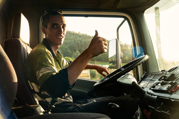 Joven diciendo que está todo bien un camión dentro de la cabina con la ropa de seguridad
 - Foto, Imagen