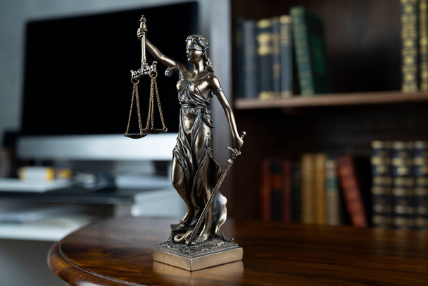 Law theme. Judge chamber. Themis statue on brown shining desk. Collection of legal books in the bookshelf. - Photo, Image