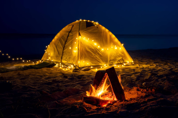 Вогонь уночі на пляжі. Літній настрій. Нічний кемпінг з ретро гірляндою на березі моря
. - Фото, зображення
