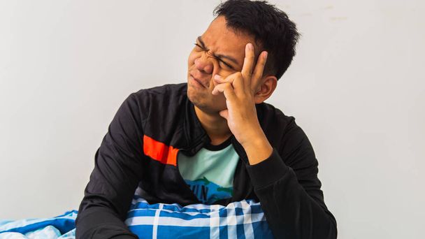 Ein Porträt eines jungen asiatischen Mannes, der Stress und drückenden Ausdruck zeigt, während er den Kopf auf dem Bett hält. - Foto, Bild