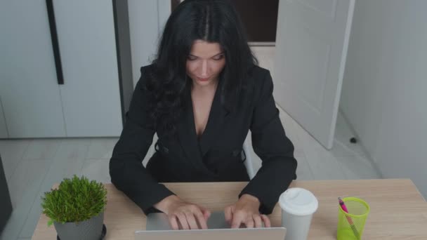 Vrouw gebruikt laptop terwijl ze aan haar bureau zit en koffie drinkt. Jonge Europese zakenvrouw zit in het kantoor en werkt aan computersoftware - Video