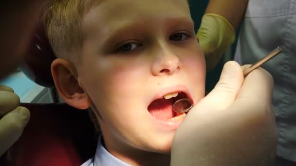 Hammashoidon käsite. lähikuva miespuolisesta hammaslääkäristä hoitamassa pientä poikaa hammashoitolassa. Lastenlääketiedettä. Hammaslääkäri tutkii hampaita poika kädessään lääketieteellisiä työkaluja. 4 k kuvamateriaalia - Materiaali, video