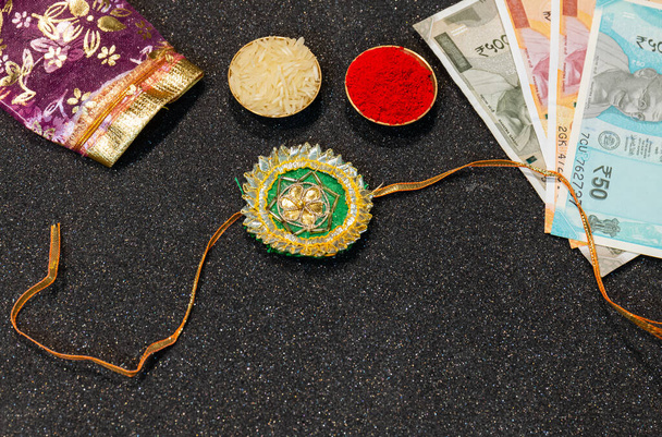 Indisches Fest, Raksha Bandhan Hintergrund mit einem eleganten bunten Rakhi, Geschenk, Reiskörner und Kumkum. Ein traditionelles indisches Armband, das ein Symbol der Liebe zwischen Brüdern und Schwestern ist. - Foto, Bild