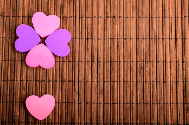 Vijf roze en paarse hartjes op een bruine bamboe tafeldecoratie, bovenaanzicht met ruimte voor tekst aan de rechterkant, selectieve focus - Foto, afbeelding