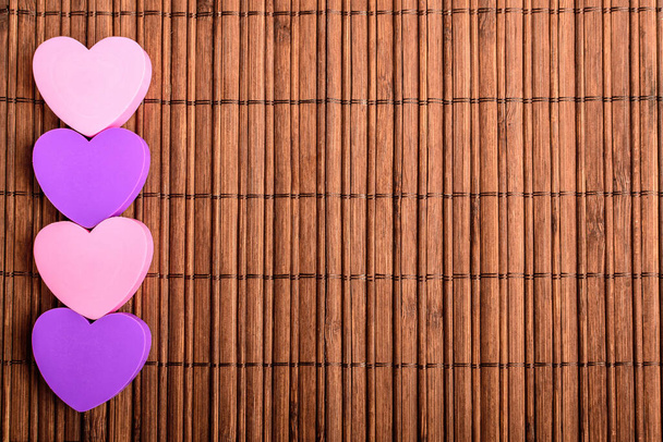Linea con quattro cuori rosa e malva su una decorazione marrone tavolo di bambù, vista dall'alto con spazio per il testo sul lato destro, messa a fuoco selettiva - Foto, immagini