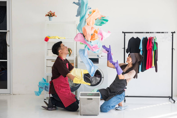 Счастливая привлекательная азиатская молодая пара бросить чистые красочные полотенца ткани после стирки на стиральной машине. Веселая жена и муж на работе по дому в выходные. - Фото, изображение