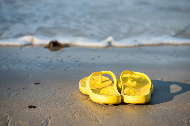 Chanclas de color amarillo o zapatos en la playa con ola de movimiento en Ao Nang, Krabi, Tailandia. sandalias en arena para divertirse viaje de vacaciones en verano en un día soleado. Vibras de vacaciones de verano
. - Foto, Imagen