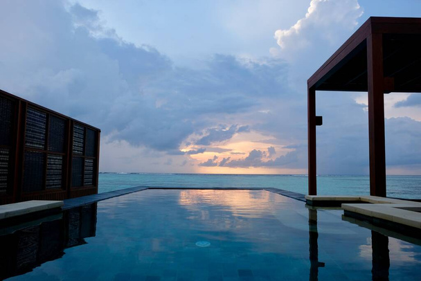 luxurious outdoor open air swimming pool. orange magnificent sunrise white cloud sky. Green wide sea horizon in Maldive island resort - Photo, Image